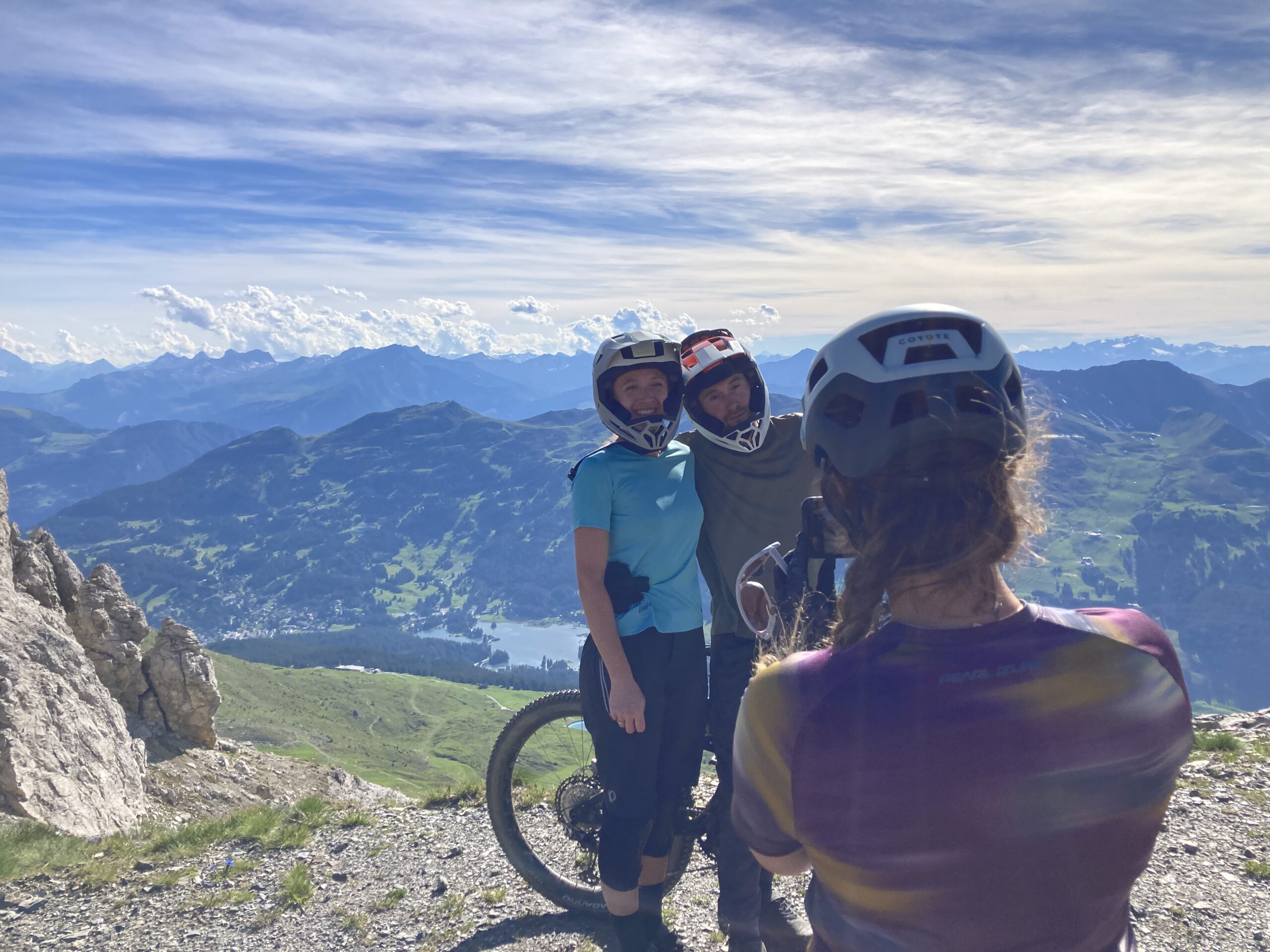 Mountain bikers wearing helmets pose for a photo against a stunning mountain backdrop, showcasing MTB helmet content production. - Alexi Hall